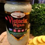 A bottle of Victoria Vegan alfredo arugula pesto next to thinly sliced potatoes and in front of kale.