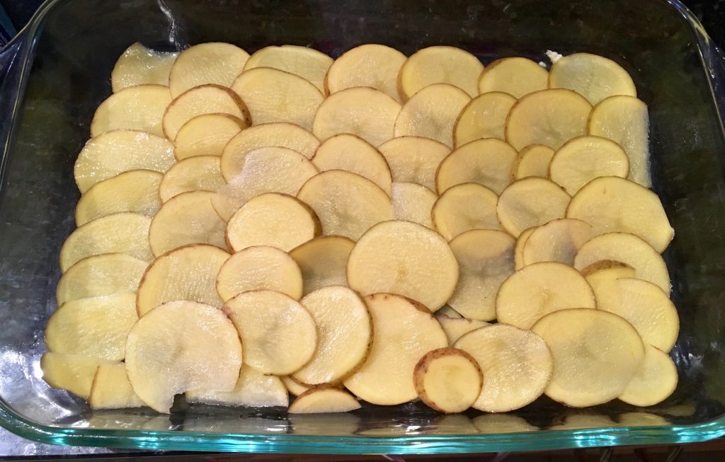 An image of thinly sliced potatoes spread out along the bottom of a glass dish.