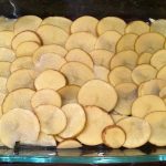An image of thinly sliced potatoes spread out along the bottom of a glass dish.