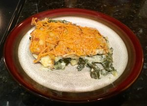 A scoop of potato and kale casserole topped with dairy free cheese on a plate. The plate is white with a brown and red rim.