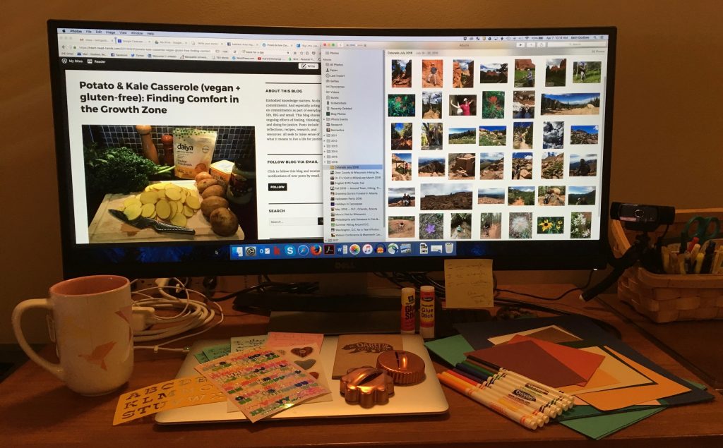 An image of desk with a large computer screen, papers, markers, glue sticks, stickers, chargers, and a laptop. On the screen is a split screen. One side has an article titled "Potato & Kale Casserole (vegan + gluten free): Finding Comfort in the Growth Zone" from Heart-Head-Hands.com. The other side of the screen is an open image library.