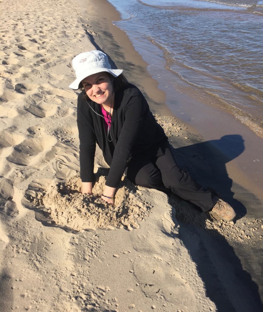 Photo of Beth along the lakeshore, dipping hands into sand.