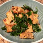 A blue, ribbed bowl containing sauteed spinach and tempeh.