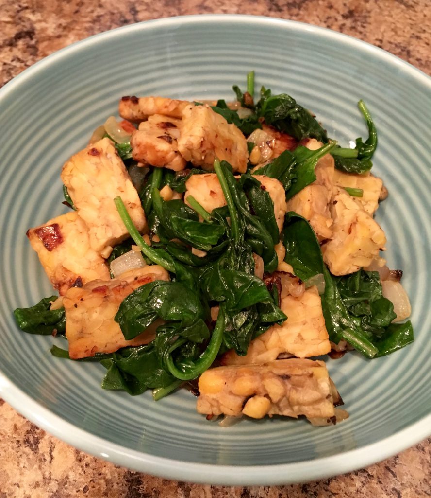 A blue, ribbed bowl containing sauteed spinach and tempeh.