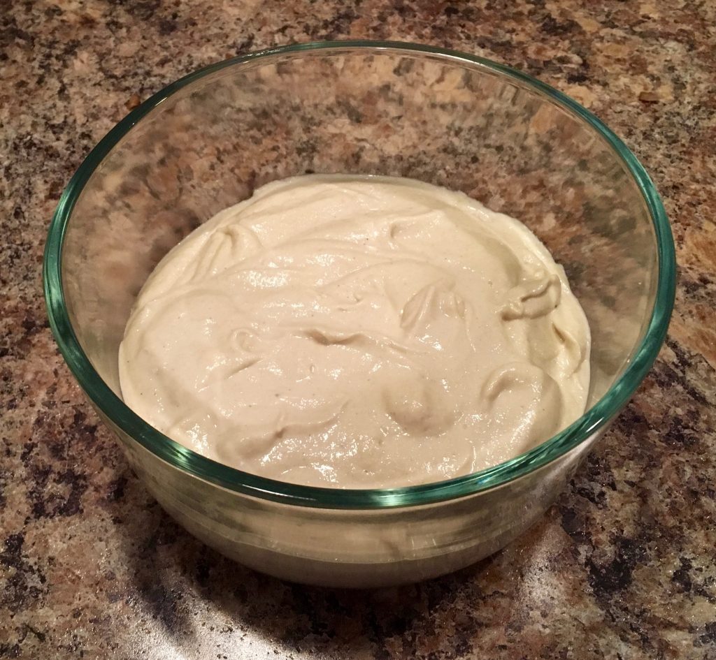 A glass bowl full of tahini sauce on a brown marble countertop.