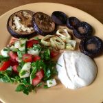 A fresh veggie salad, roasted mushrooms and onions, and tahini sauce on a beige plate on a wooden surface.