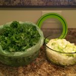 A bag of fresh kale and a glass container containing a medley of celery and onion sit on a brown countertop.