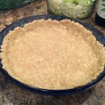 A blue pie dish is lined with light brown pie crust and sits on a countertop.