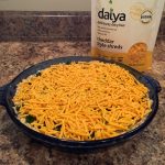 An uncooked savory pie sits next to a bag of dairy free cheddar cheese on a brown marble countertop.