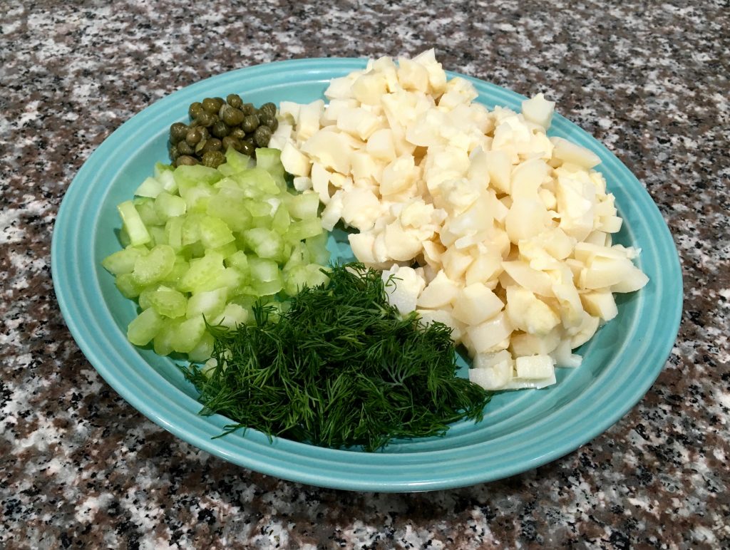 A blue plate with hearts of palm, fresh dill, chopped celery, and capers on the plate.