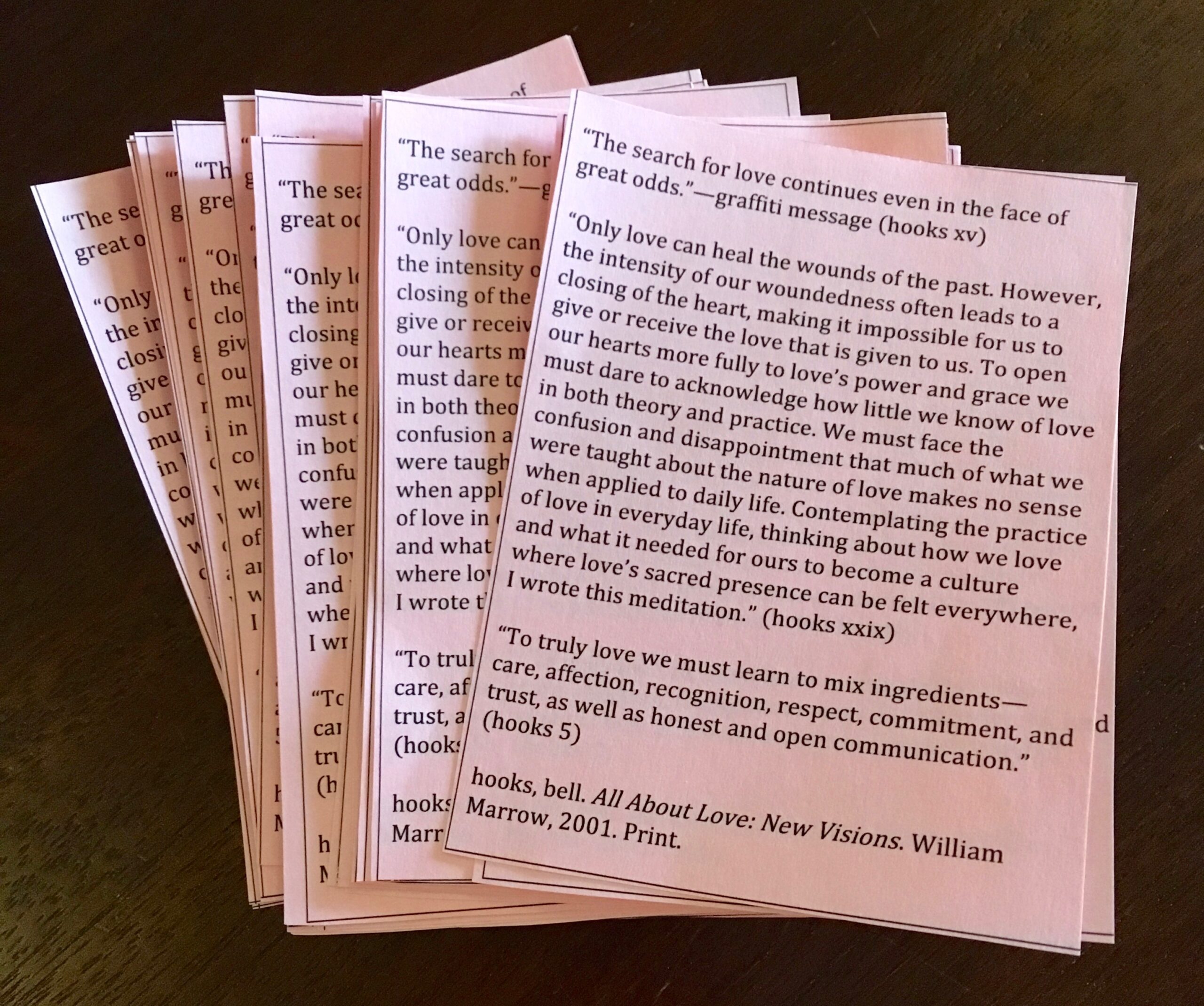 A stack of small pink papers with messages from bell hooks' "All About Love: New Visions."