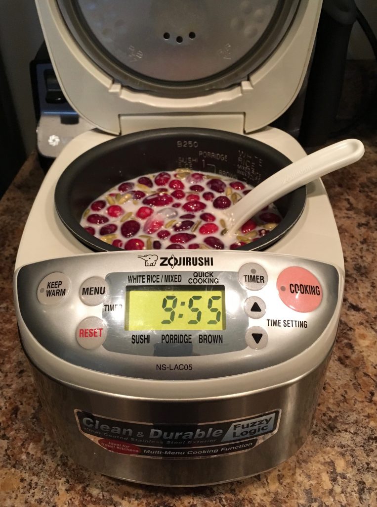 A rice cooker containing the uncooked ingredients for warm quinoa cranberry breakfast cereal.