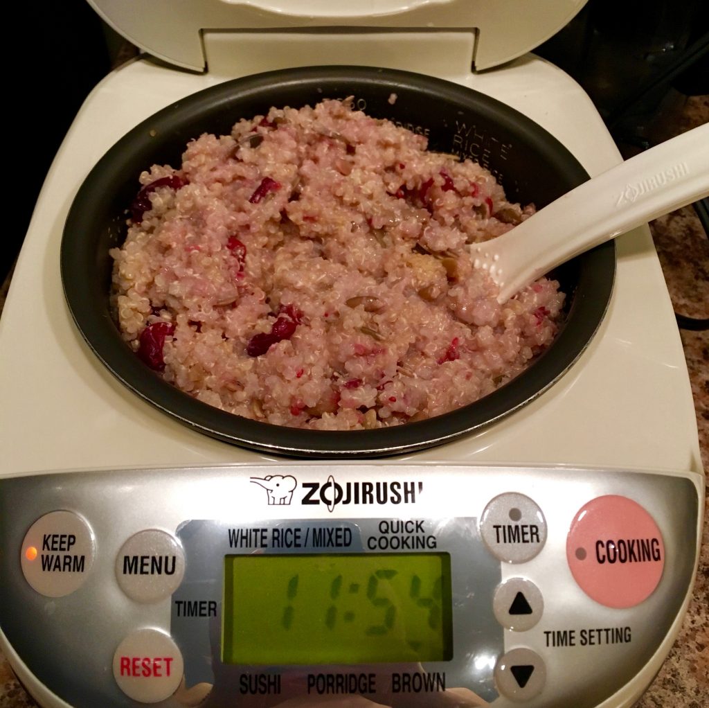 A rice cooker containing warm quinoa cranberry breakfast cereal with a plastic, white ladle sticking out.