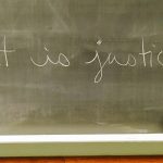 "What is justice?" written in white chalk on a black chalkboard.