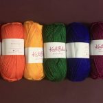 Skeins of yarn laid in a row: red, orange, yellow, green, blue, plum, purple.