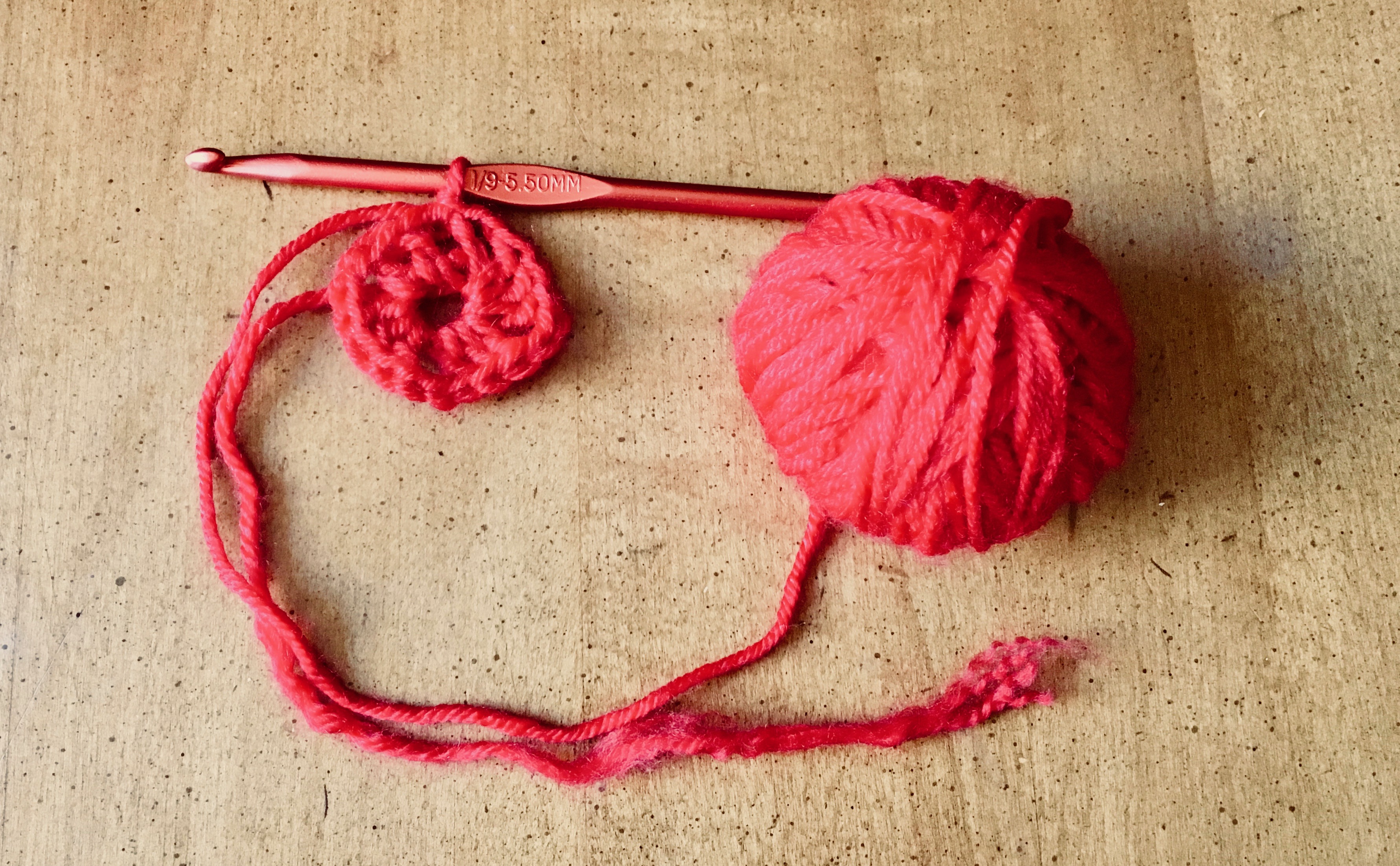 Red yarn crocheted into the center round for a granny square to emerge.