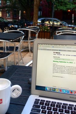 Image from an outdoor café. In the foreground are a vegan tea latte and laptop open to the writing website 750words.com. In the background appear metal chairs and tables inside a metal fence. Beyond the café are cars, trees, and row houses.
