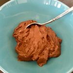 The pudding is prepared and appears centered in a blue bowl with a metal spoon inserted, its handle stretching beyond the photo’s edge.