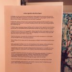 Printed copy of the spell (words that appear in this blog post) taped to a bathroom mirror with a colorful shower curtain showing part of a tree reflected in the mirror. The photo has a pink tint.