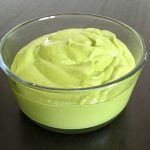 Green pesto sauce appears in a clear glass container against a black table top.