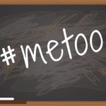 This images shows the #metoo hashtag in white script printed diagonally on a blackboard with messy erasure marks in the background.