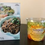 This image shows two packaged items by Trader Joe’s sitting side-by-side: on the left are a box steamed lentils, and on the right a circular plastic container of Mirepoix (chopped celery, carrots, and onions).