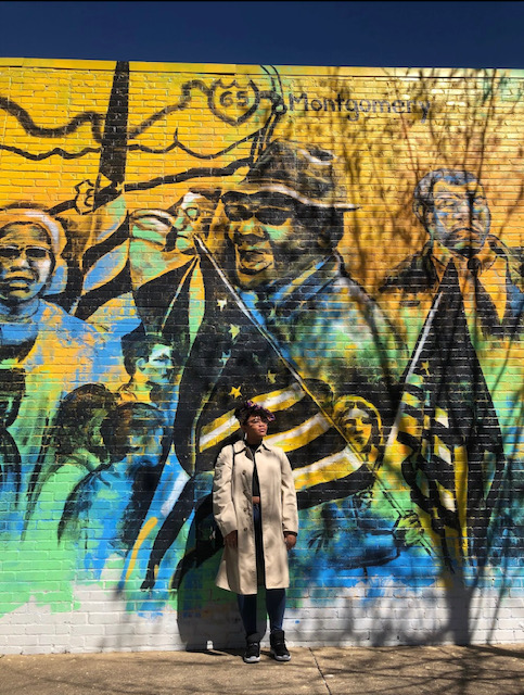 Photo of Alexa Eason standing against a mural on the Civil Rights Trail in Montgomery, Alabama.