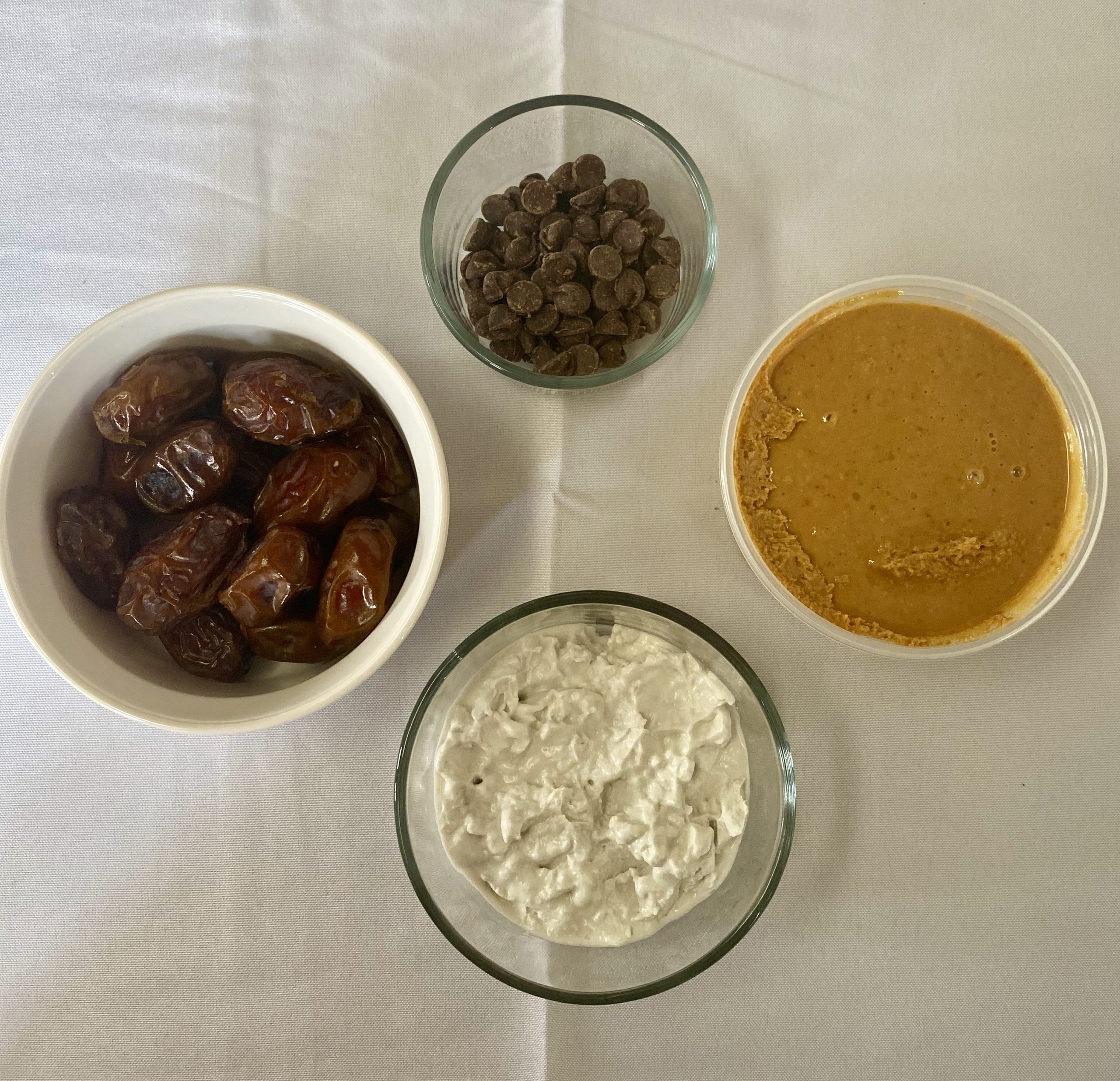 Ingredients for vegan stuffed dates (moving clockwise): fresh Medjool dates, semi-sweet chocolate chips, peanut butter, and coconut cream.
