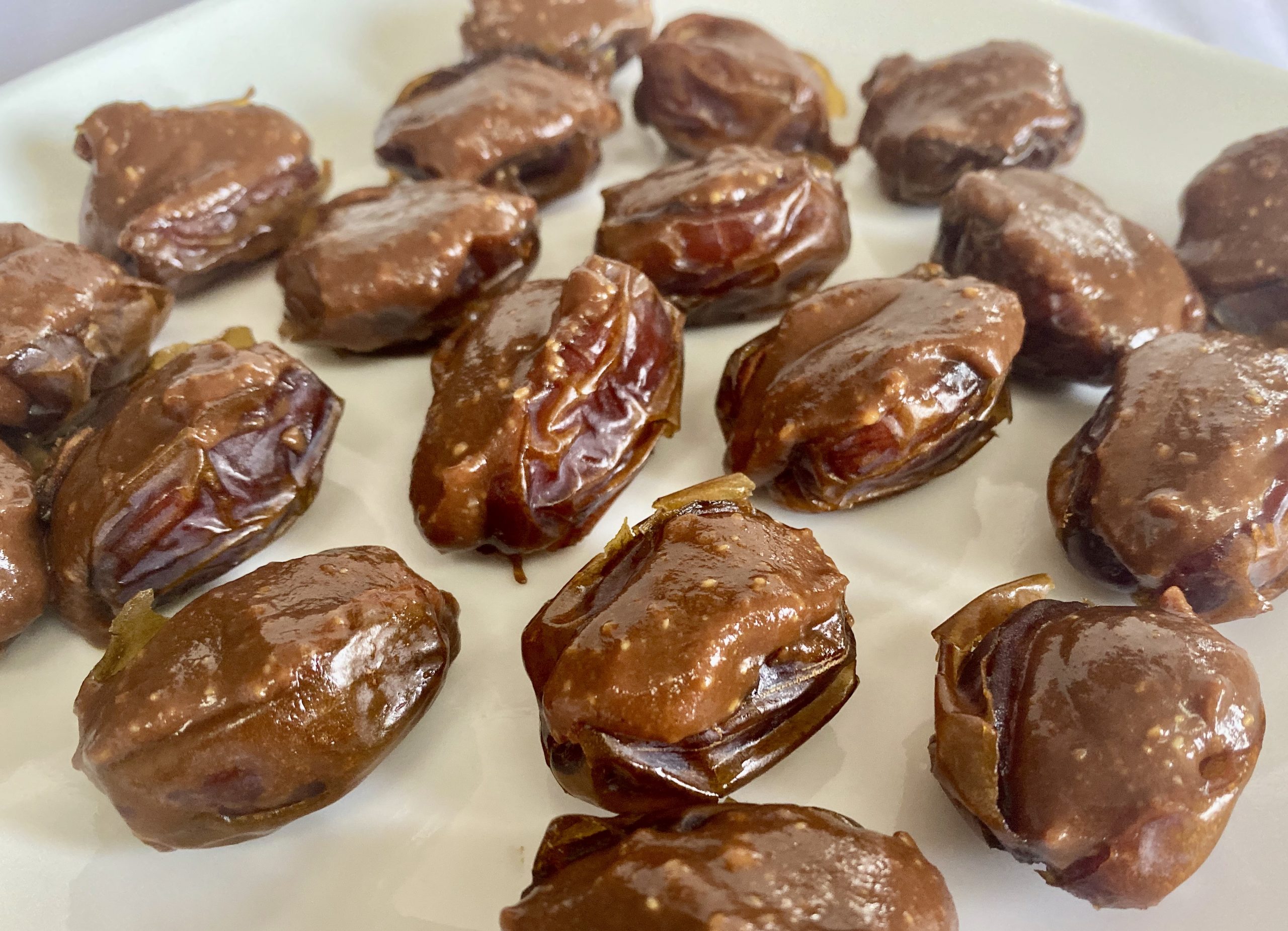 This image shows the gooey goodness of vegan and gluten-free stuffed dates with the creamy, chocolaty mixture spilling over the top and with small bits of peanuts visible.