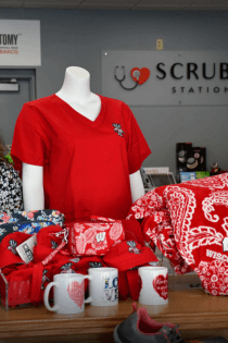 This image shows Ileana Rodriguez standing next to UW-Madison Badger clothing and mugs (all red and white) inside Scrubs Station in Madison, Wisconsin.