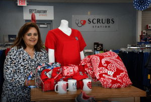 This image shows Ileana Rodriguez standing next to UW-Madison Badger clothing and mugs (all red and white) inside Scrubs Station in Madison, Wisconsin.