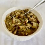 This image shows vegan flourless mushroom gravy with pieces of onion and mushroom in a brown sauce—in a white bowl, surrounded by a white cloth.