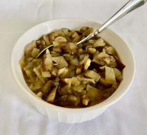 This image shows vegan flourless mushroom gravy with pieces of onion and mushroom in a brown sauce—in a white bowl, surrounded by a white cloth.