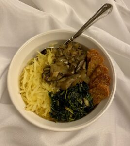 This vegan and gluten-free dinner bowl shows mushroom gravy, along with spaghetti squash, sautéed greens, and tempeh sticks.