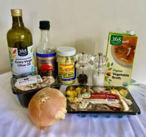 This image shares ingredients. From left to right: olive oil, tamari, chicken style vegan seasoning, pepper, salt, vegetable broth. In the front: an onion and mushrooms.