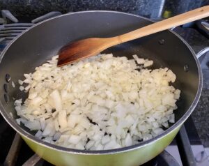 A large frying pan contains chopped white onions sautéing.