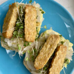 Tempeh sticks cover open-faced sandwiches of mashed avocado, sour kraut, and microgreens and on ciabatta buns.