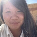 This image shows Chloe wearing a white shirt, with hair to one side, smiling. Rays of sunlight frame her face and highlight the smile.