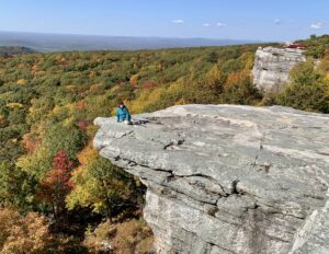 This photo (from recent hiking in New York) shows me sitting on a cliff’s edge, surrounded by fall colors: trees in various shades of green, yellow, orange, and red. I share this photo because it feels like I’m on edge right now, nearing something new.