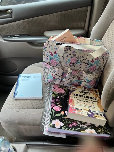 Candace’s mobile office: the backseat of the van covered by a carrier, paper, pens, a notebook, and book Craft and Conscience: How to Write about Social Issues.