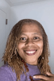 A photo of Pam Jones smiling at the camera in a purple sweater and red stone necklace.